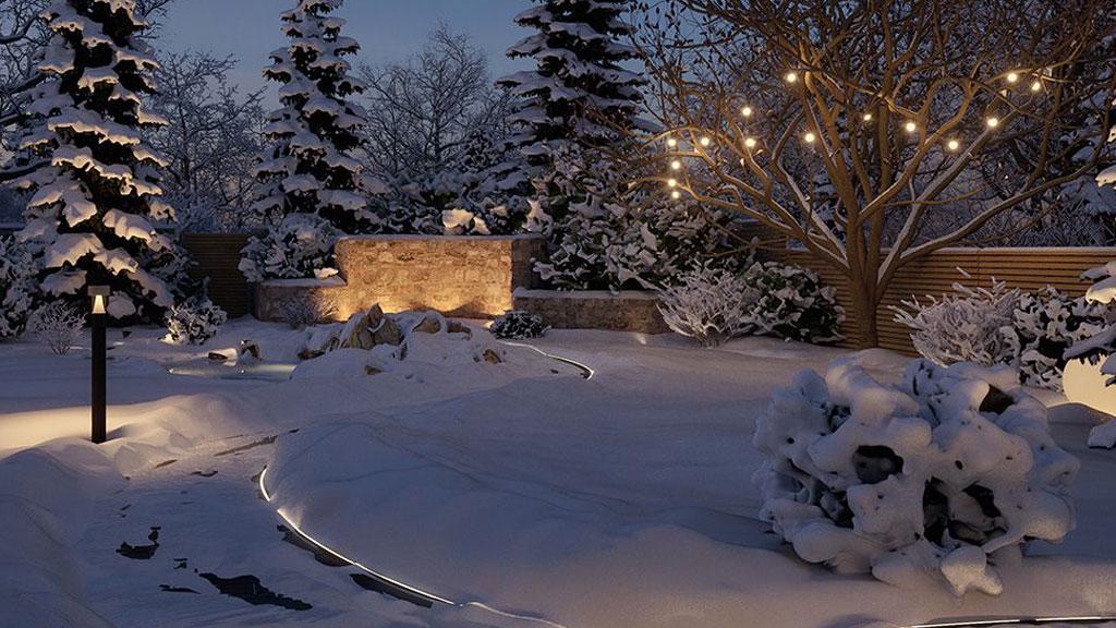 Winter garden scene with snow-covered trees and warm white LED outdoor lighting for terrace and paths.