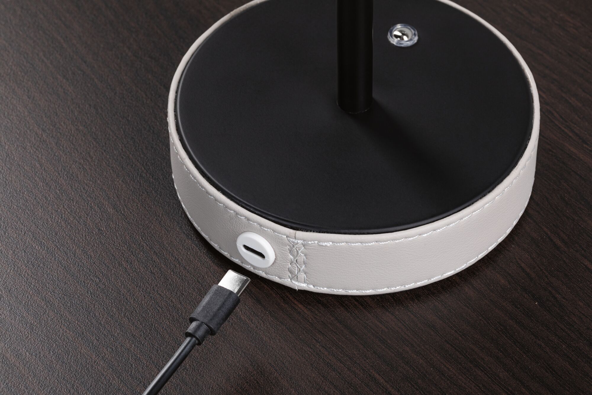Runder Lampenfuß mit schwarzer Oberfläche und weißem Lederbezug mit USB-C Anschluss auf dunklem Holztisch