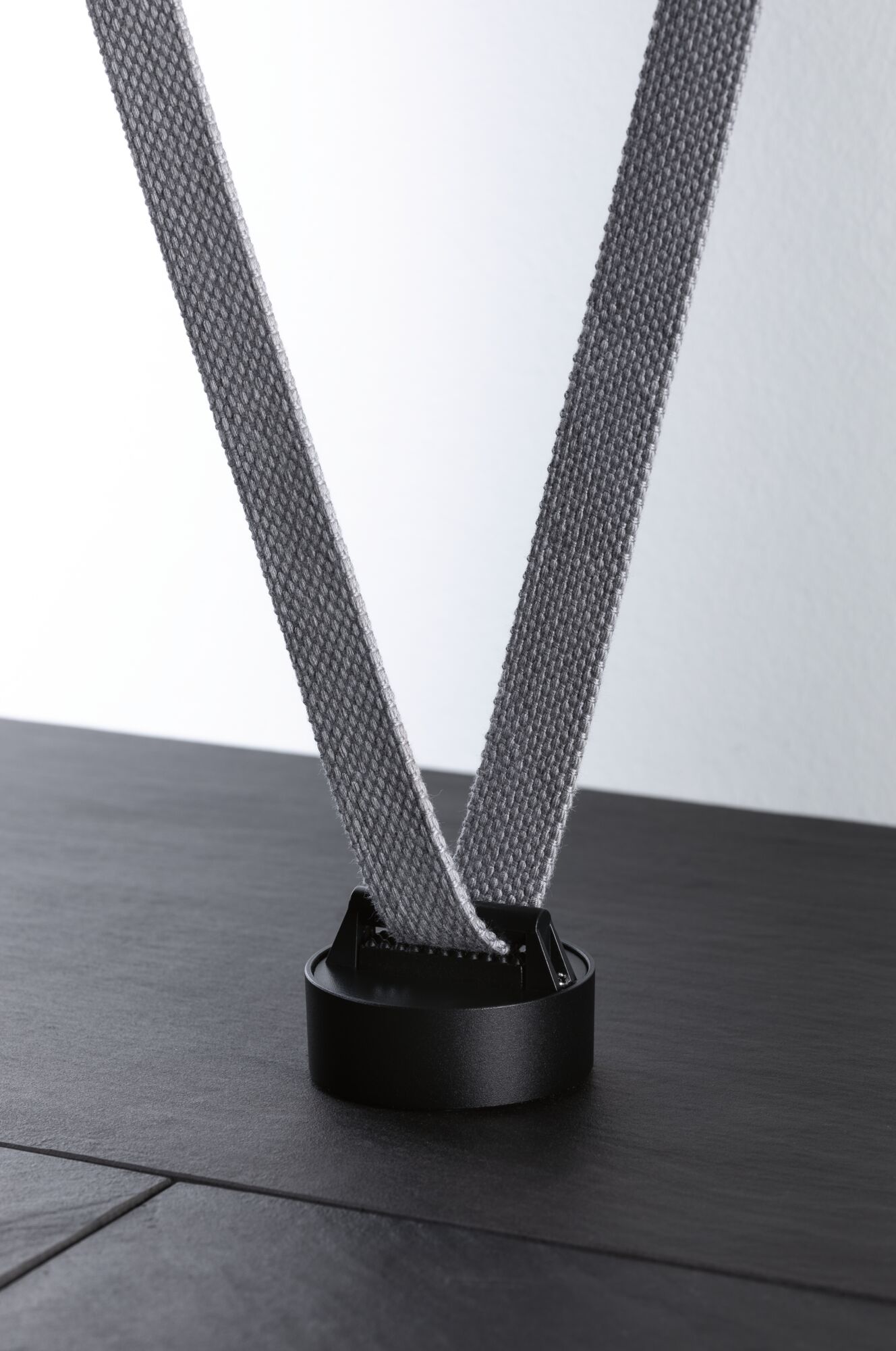 Black round holder with grey fabric strap on dark surface for lighting system accessories
