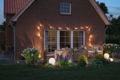 Cozy terrace with round white LED light spheres and warm string lights on red brick wall at dusk.