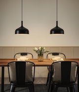 Zwei schwarze Metall-Hängeleuchten über Holztisch mit gedecktem Platz und Blumenvase im Esszimmer
