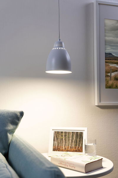 Grijze metalen hanglamp met geperforeerd patroon die warm licht geeft boven een wit bijzettafeltje met boek en glas.