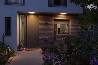 Moderner Hauseingang mit warmweißer LED-Außenbeleuchtung und blühendem Garten im Abendlicht