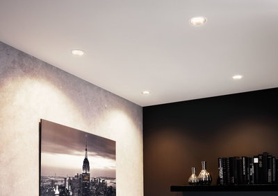 Quatre spots LED encastrés blancs au plafond éclairent un salon moderne avec mur noir et photo urbaine.