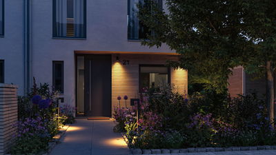 Beleuchteter Hauseingang mit moderner Außenbeleuchtung und blühendem Garten im Abendlicht
