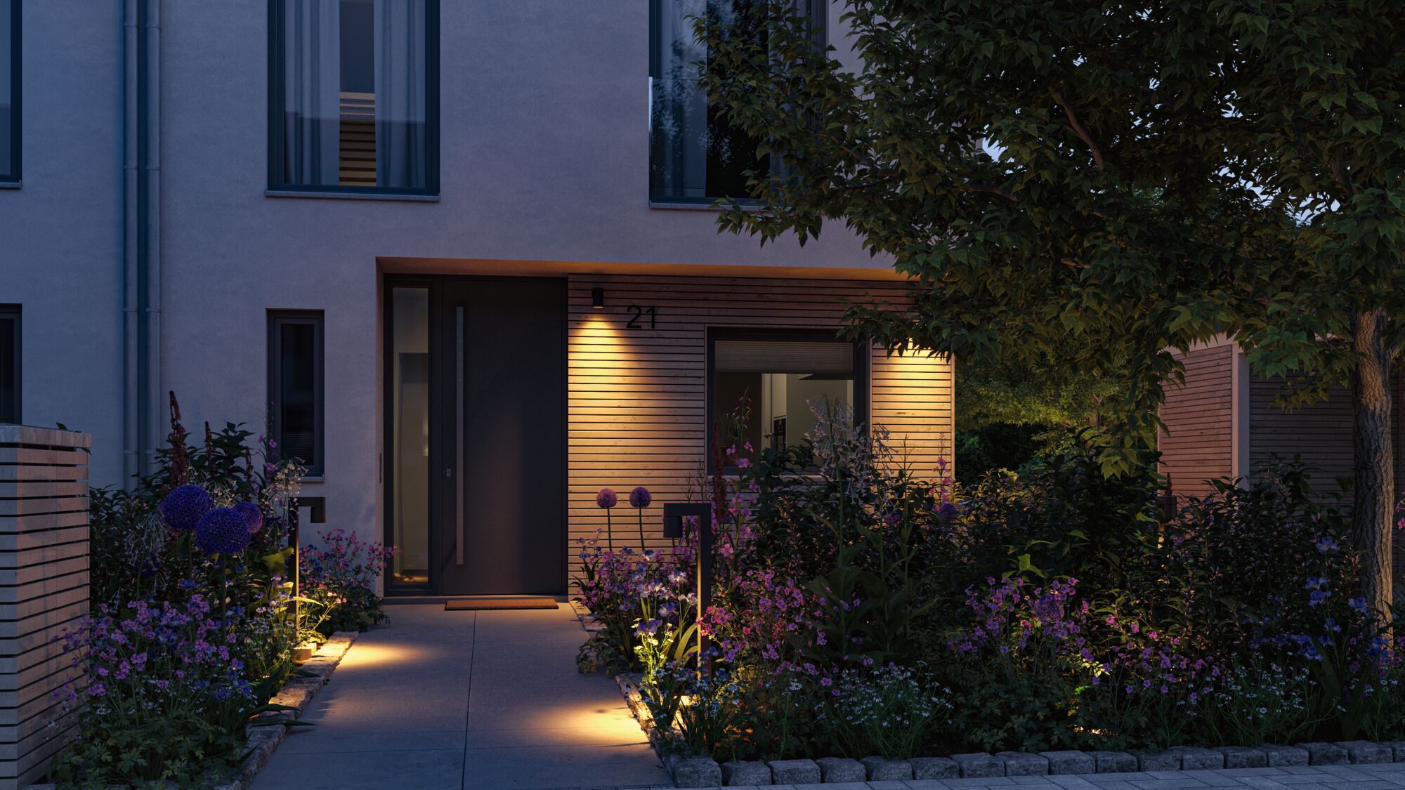 Oplyst husindgang med moderne udendørsbelysning og blomstrende have ved skumring