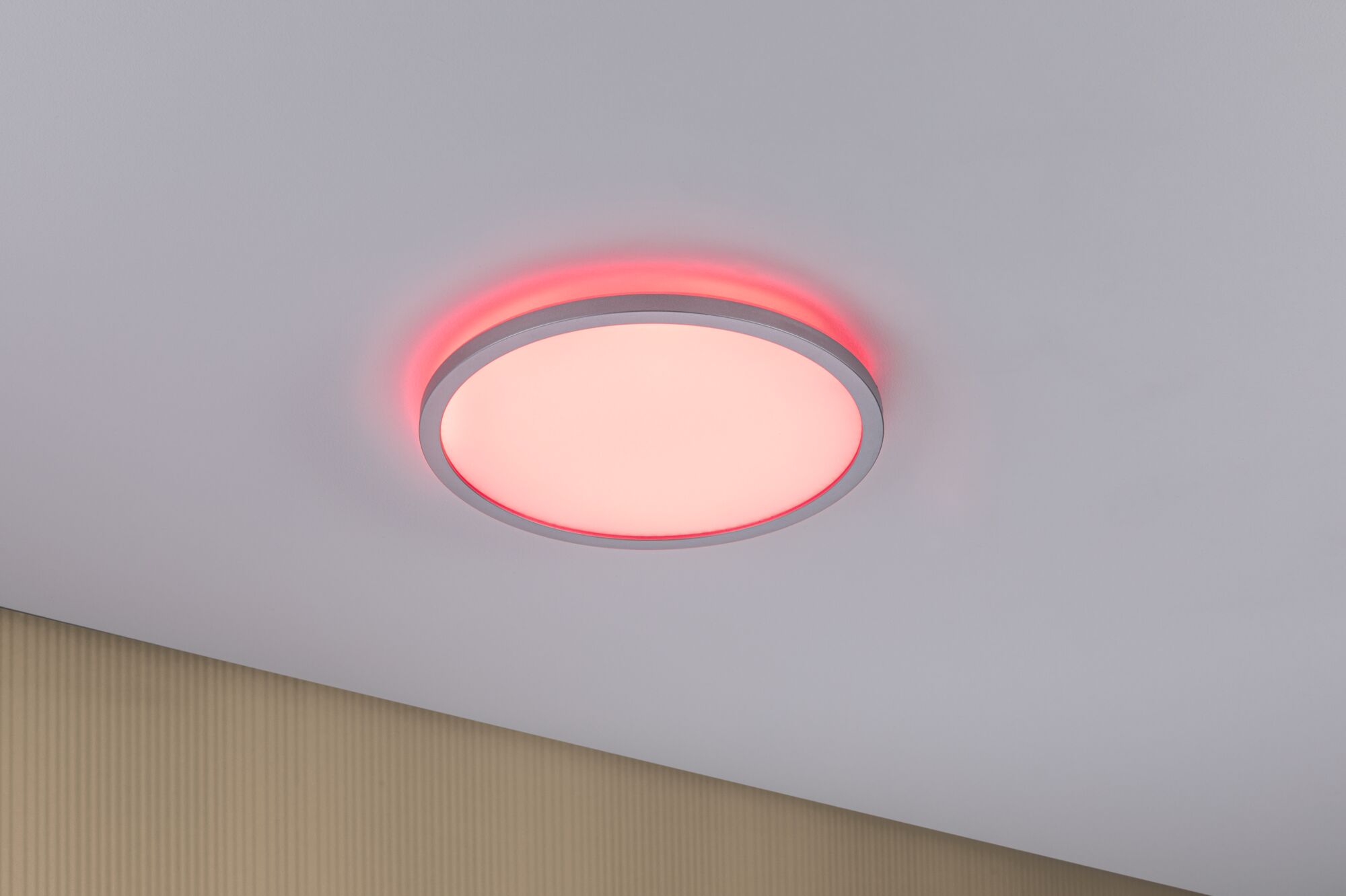 Runde LED-Deckenleuchte mit weißem Diffusor und rotem Lichtakzent an der Wand für modernes Ambiente