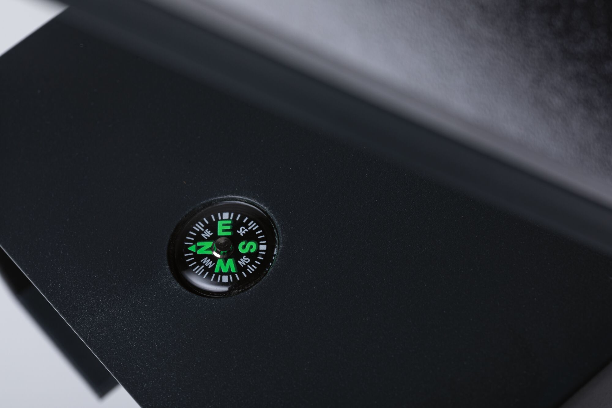 Small green compass in black casing on matte black surface for precise navigation and orientation