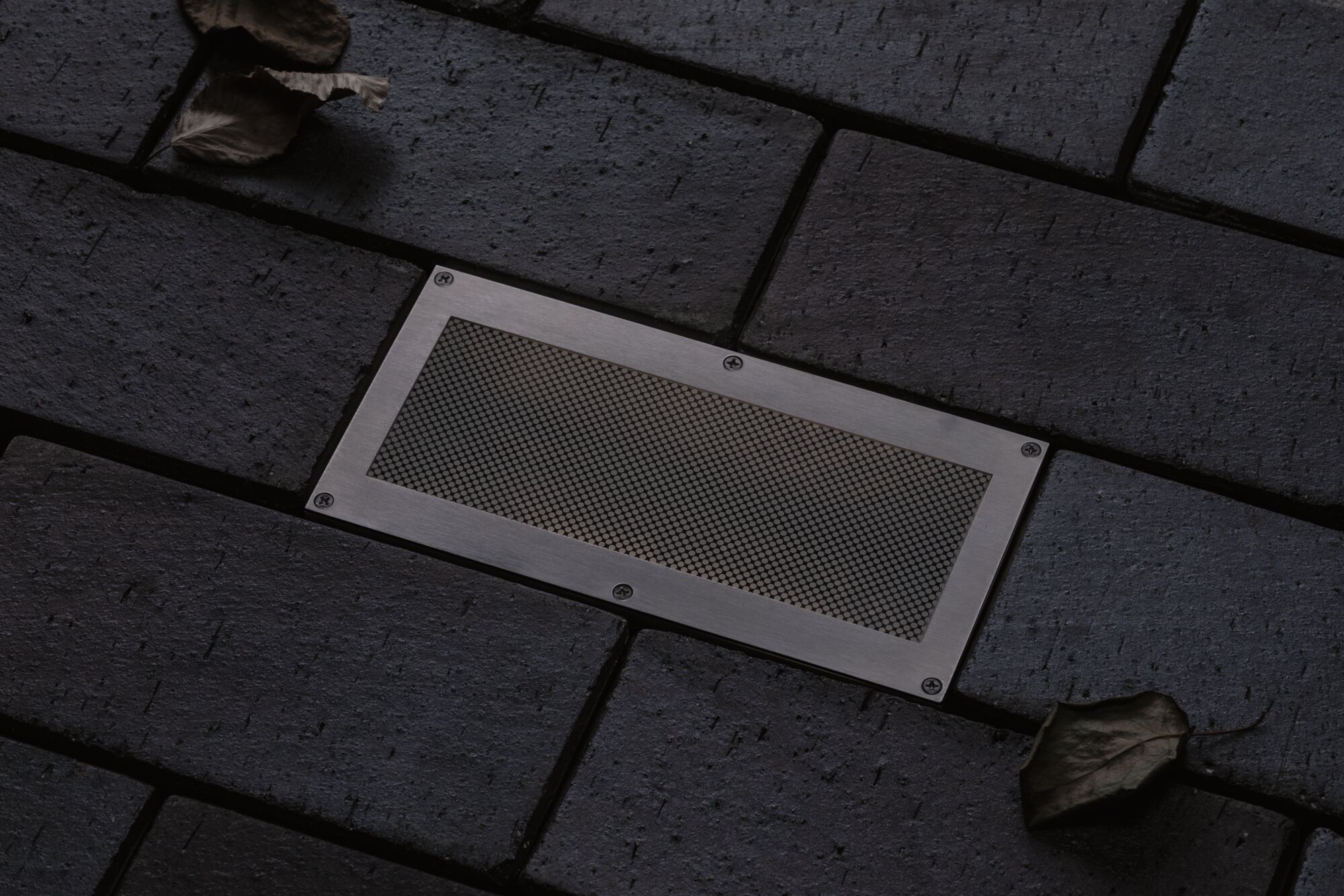 Rectangular stainless steel floor spotlight with mesh insert in dark pavement for outdoor lighting
