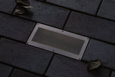 Rectangular stainless steel floor spotlight with mesh insert in dark pavement for outdoor lighting