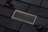 Projecteur de sol rectangulaire en acier inoxydable avec grille intégré dans pavé sombre extérieur