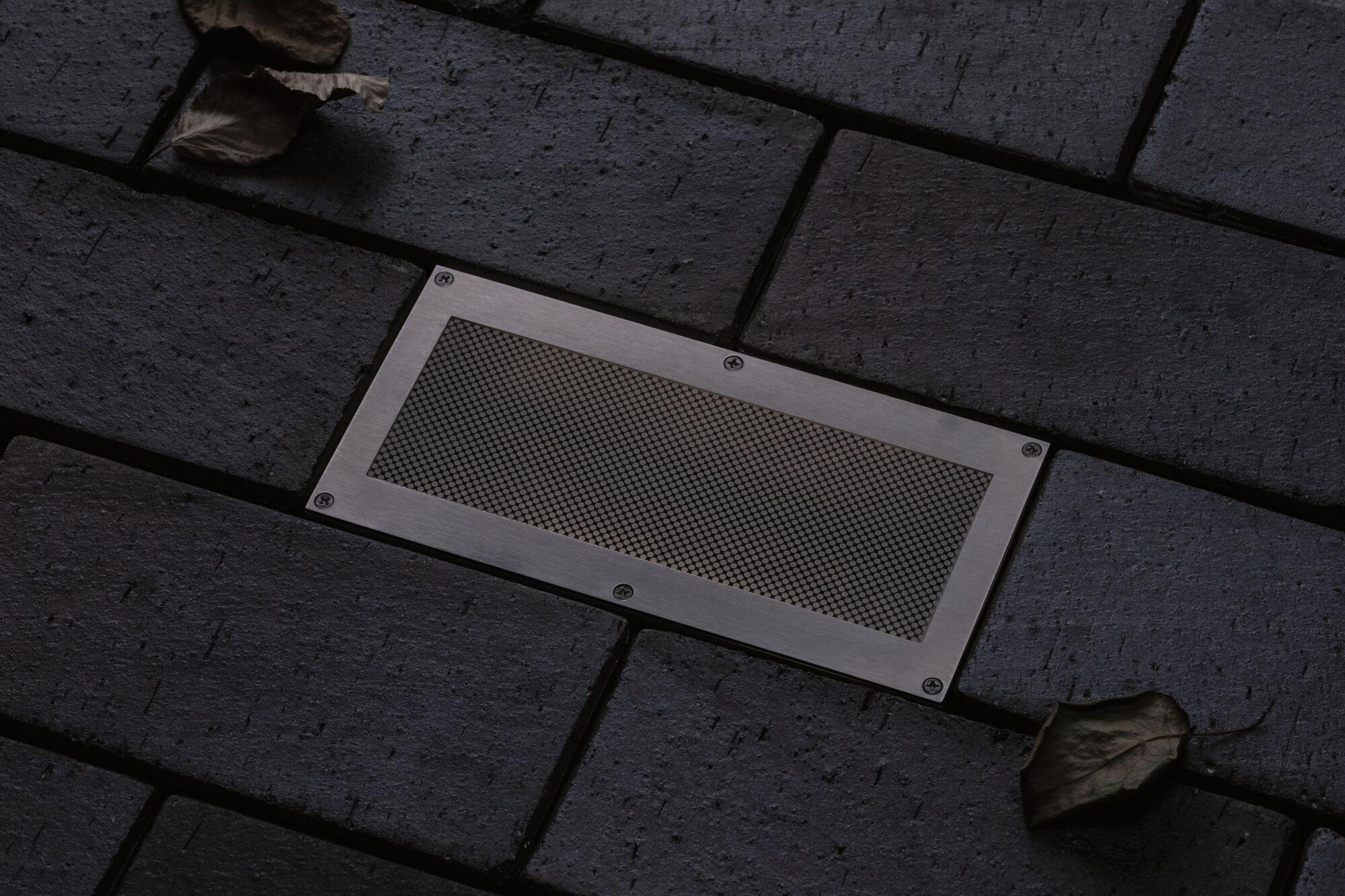 Rectangular stainless steel floor light with mesh on dark paving for outdoor lighting solution