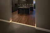 Moderne keuken met donkere kasten, houten vloer en LED-vloerverlichting bij de overgang.