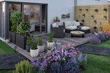 Jardin moderne avec salon gris, terrasse en bois, pots de plantes et fleurs colorées pour éclairage extérieur.