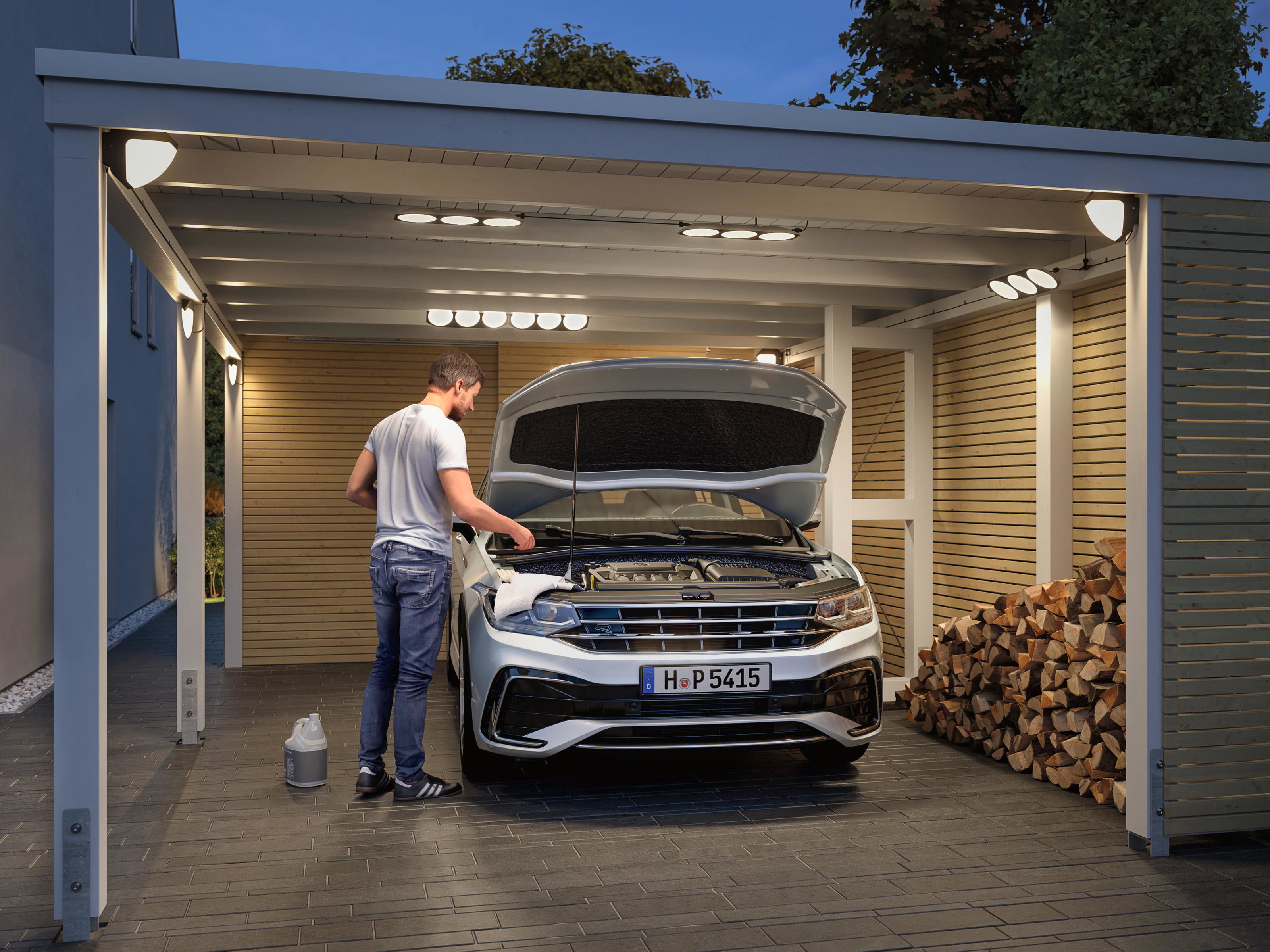 Beleuchteter Carport mit moderner LED-Deckenbeleuchtung und Mann, der Auto mit geöffneter Motorhaube wartet.