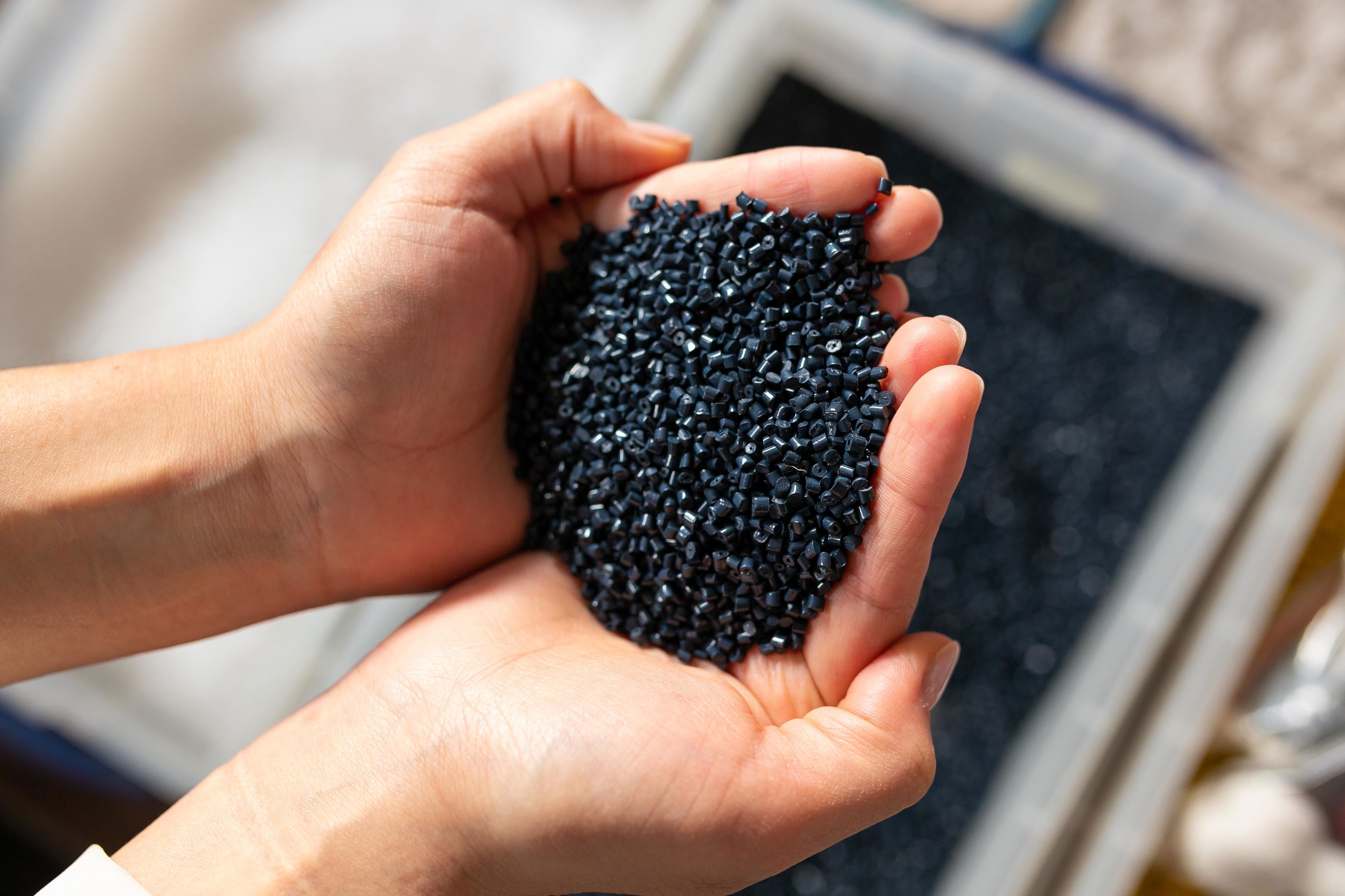 Hands holding black plastic granules as sustainable recycled material for eco-friendly products