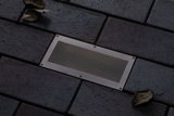 Spot de sol rectangulaire en acier inoxydable avec grille intégré dans pavé foncé pour éclairage extérieur.