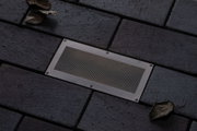 Recessed stainless steel floor light with mesh insert on dark paving for outdoor lighting