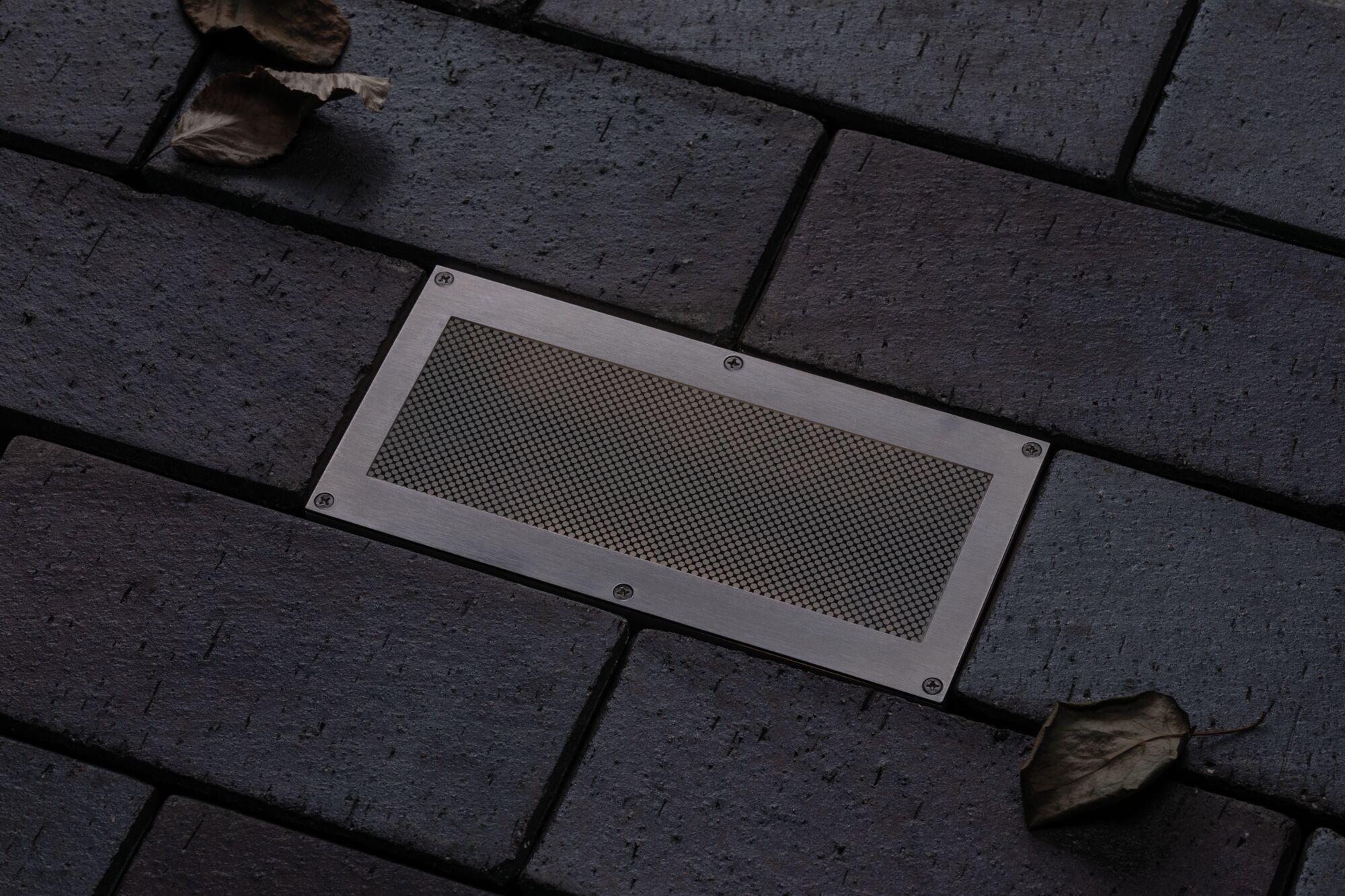 Recessed stainless steel floor light with mesh insert on dark paving for outdoor lighting