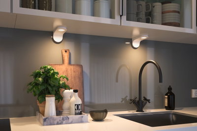 Modern kitchen countertop with black faucet, marble tray, and LED under-cabinet lights.