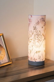Zylindrische Tischlampe mit floralem Stoffschirm in Pastellfarben auf Holztisch für Wohnraumbeleuchtung