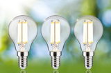 Drei klare LED-Glühbirnen mit E14-Fassung und warmweißem Licht vor unscharfem grün-blauem Hintergrund