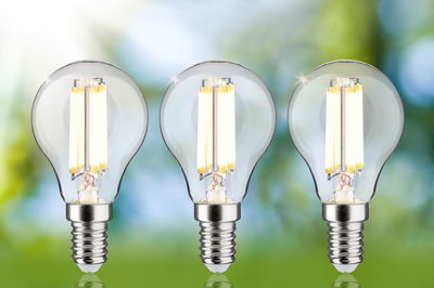 Drei klare LED-Glühbirnen mit E14-Fassung und warmweißem Licht vor unscharfem grün-blauem Hintergrund