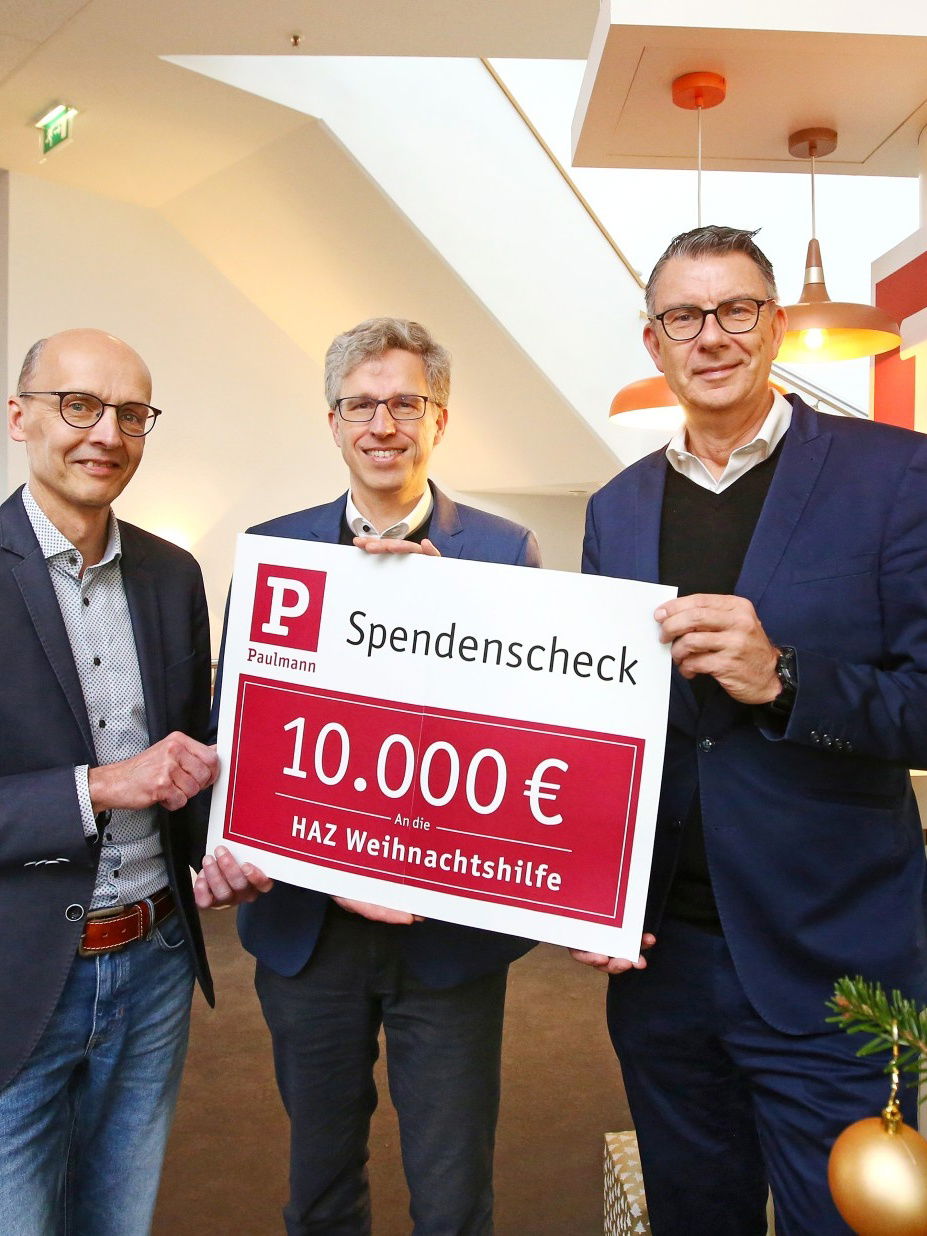 Drei Männer in Anzügen halten einen Spendenscheck über 10.000 Euro für HAZ Weihnachtshilfe in Büro.