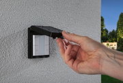 Hand lifting black rain cover with water drops over white outdoor light switch on textured wall