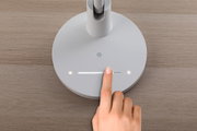 Vinger bedient witte ronde LED-bureaulamp met touchdimmer op houten oppervlak