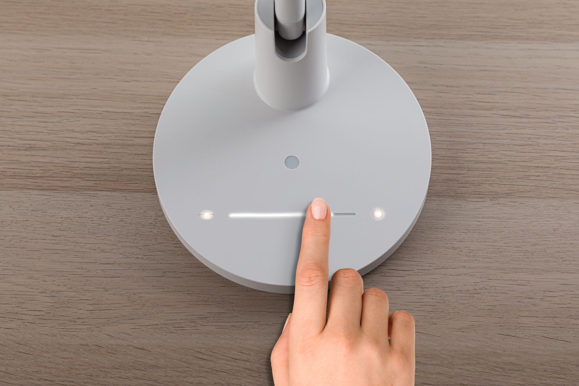 Vinger bedient witte ronde LED-bureaulamp met touchdimmer op houten oppervlak