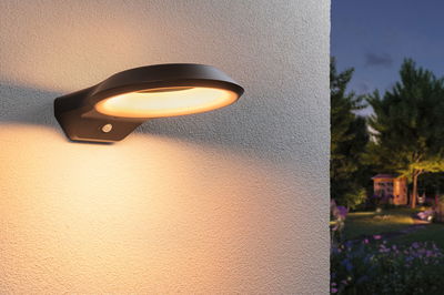 Schwarze LED-Außenwandleuchte mit warmweißem Licht und Bewegungsmelder an Hauswand bei Dämmerung