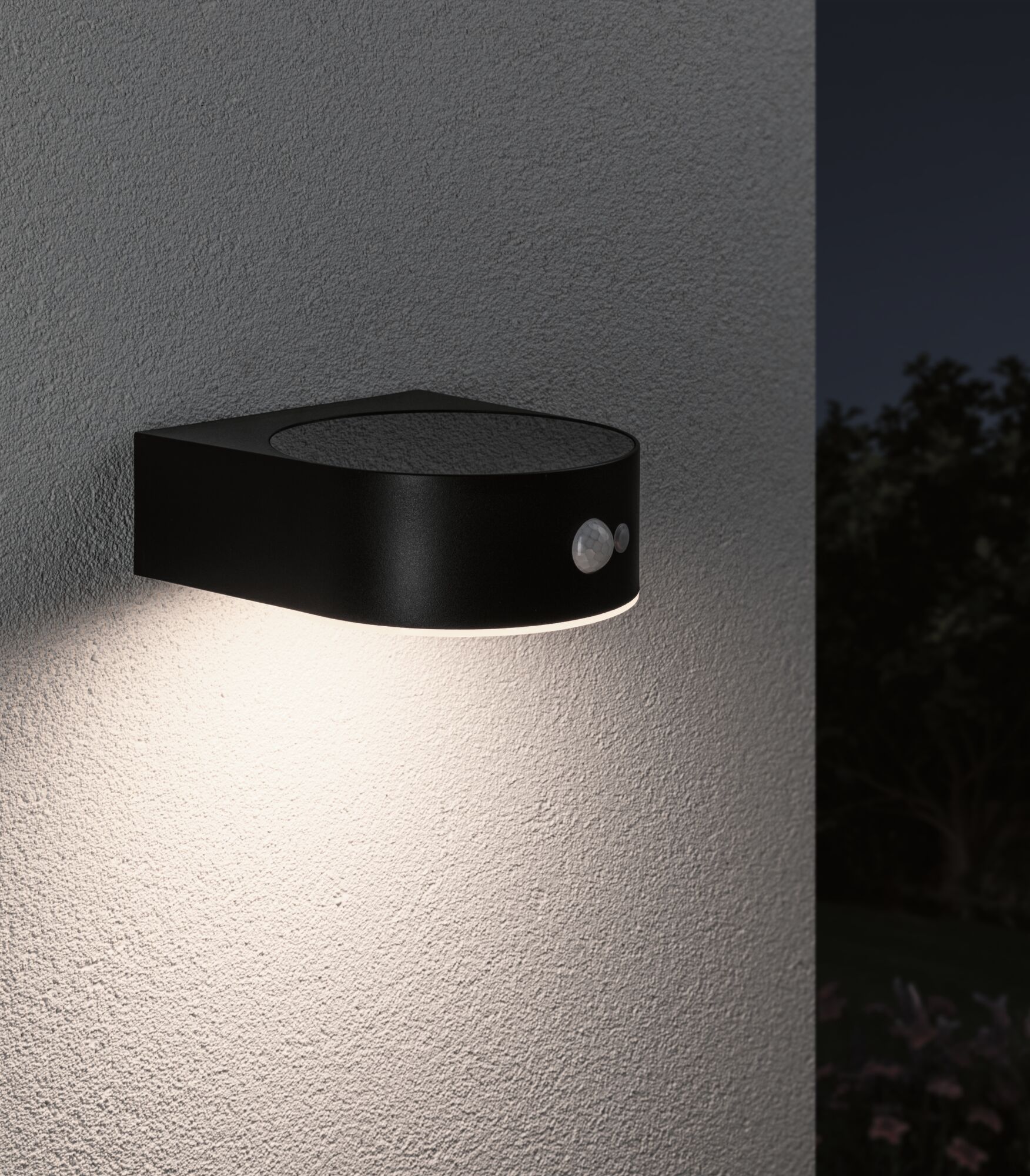 Zwarte metalen buitenwandlamp met bewegingssensor en warm wit licht op grijze muur