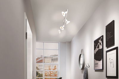 Moderne witte plafondspot met vier verstelbare lampen in lichte gang met raam en wanddecoratie