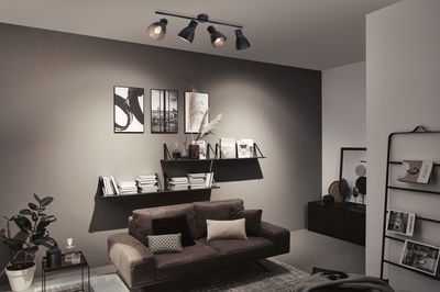 Schwarze Deckenleuchte mit vier verstellbaren Spots in modernem Wohnzimmer mit braunem Sofa.