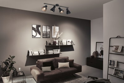 Plafonnier noir avec quatre spots réglables dans un salon moderne avec canapé marron.
