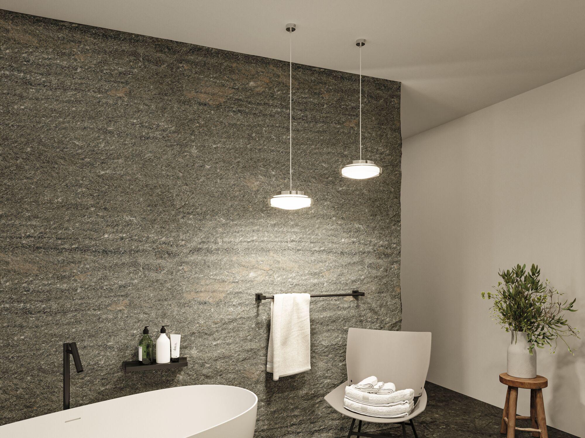 Salle de bain moderne avec baignoire blanche autoportante, mur en pierre naturelle grise et deux suspensions LED rondes.