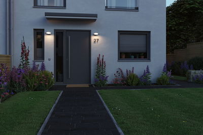 Modern house facade with grey front door, illuminated outdoor wall lights, and neat garden path.