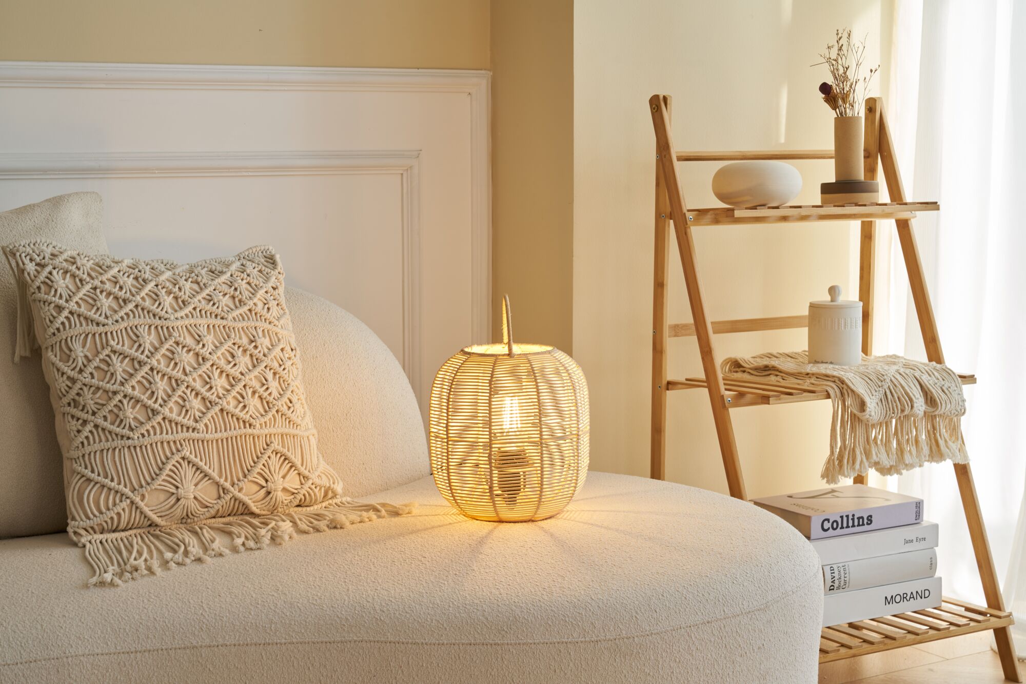 Round rattan table lamp with warm light on cream sofa beside macrame cushion and wooden shelf