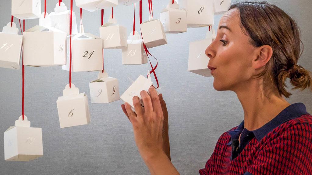 Frau betrachtet weißen Adventskalender aus Papierwürfeln mit roten Bändern, Weihnachtsdeko Idee.