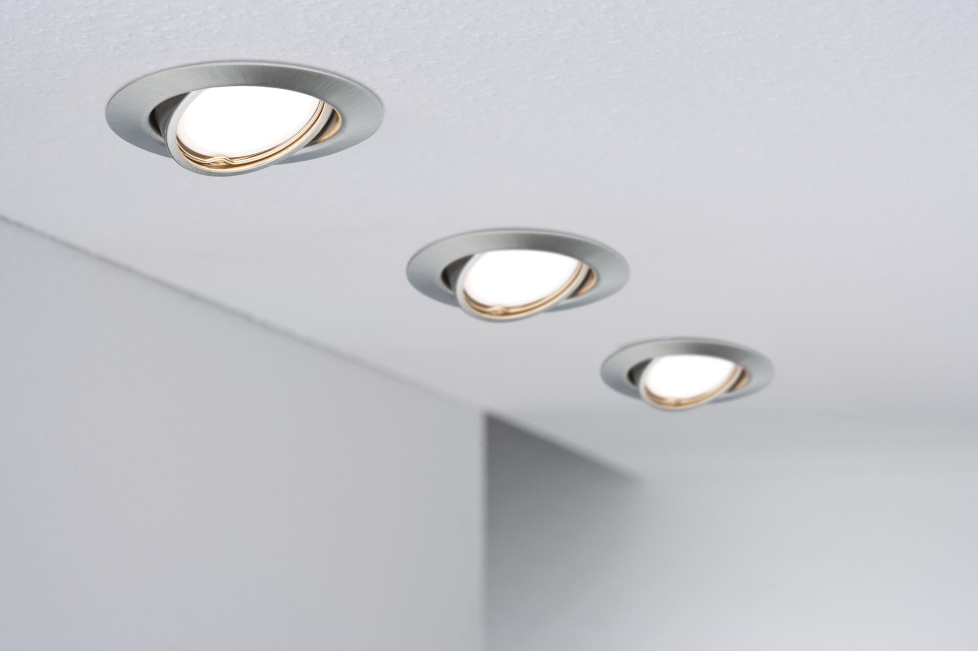 Trois spots encastrés orientables en aluminium brossé installés au plafond pour éclairage moderne