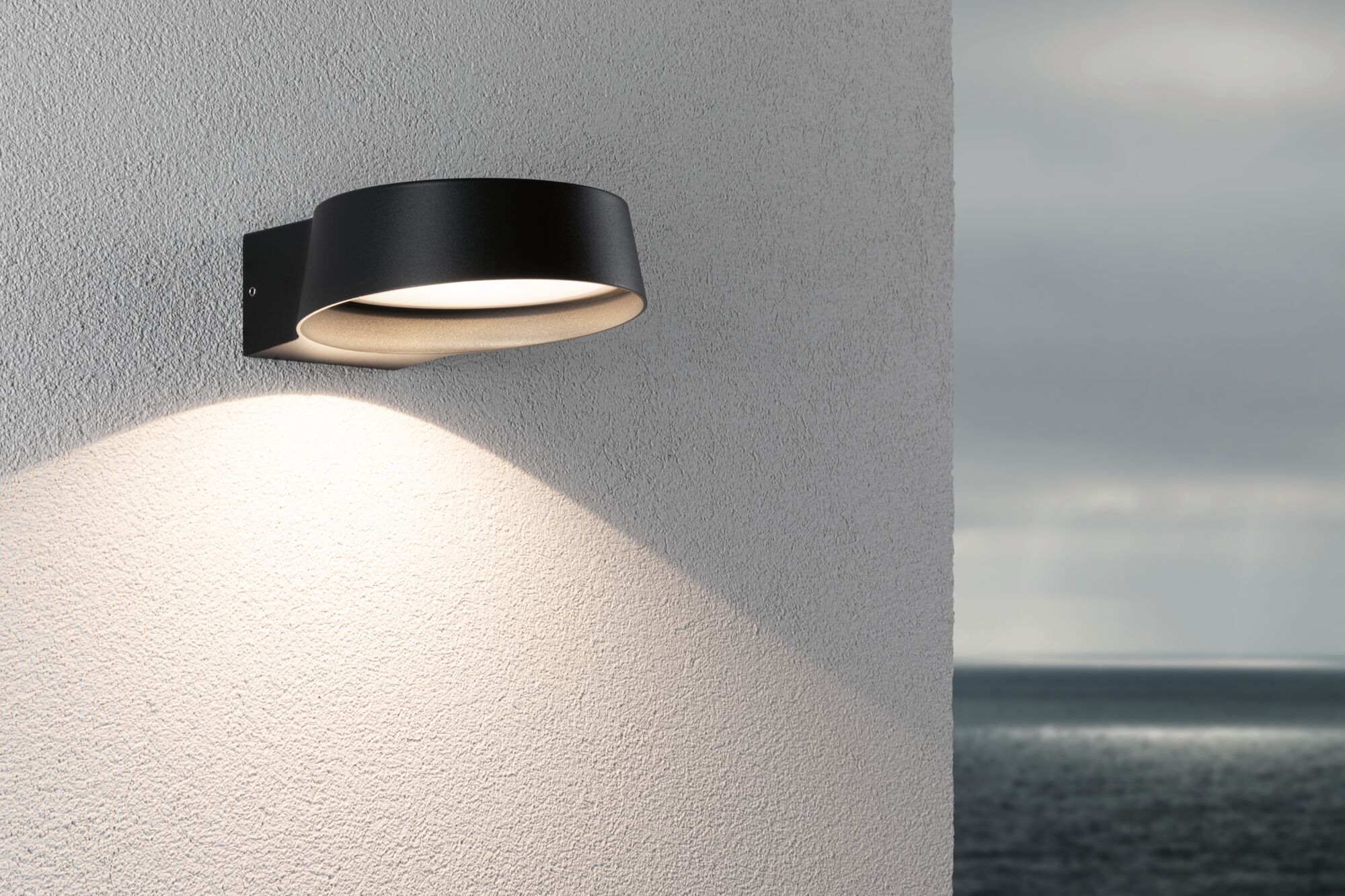 Moderner schwarzer Aluminium-Wandleuchter mit warmweißem LED-Licht an Außenwand mit Meerblick
