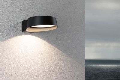 Moderner schwarzer Aluminium-Wandleuchter mit warmweißem LED-Licht an Außenwand mit Meerblick