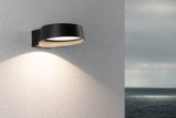 Moderner schwarzer Aluminium-Wandleuchter mit warmweißem LED-Licht an Außenwand mit Meerblick