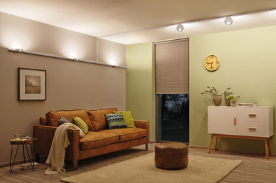 Salon moderne avec canapé en cuir marron, tapis, buffet blanc, éclairé par des spots LED au plafond