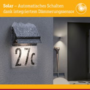 Schwarze Solar-Hausnummernleuchte mit integriertem Dämmerungssensor und Schneebedeckung an grauer Wand