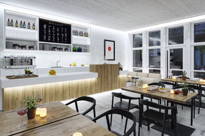 Modern café interior with wooden counter, white tiles, black chairs, and warm LED lighting for cozy ambiance