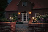 Two black metal outdoor lamps on red brick walls lighting a house entrance at dusk