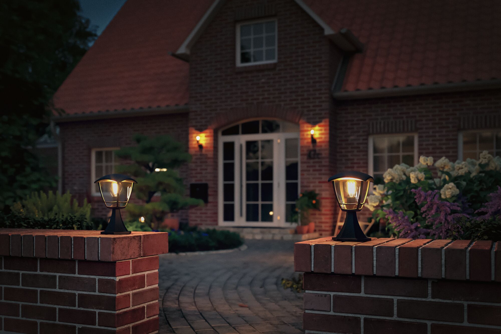 Two black metal outdoor lamps on red brick walls lighting a house entrance at dusk