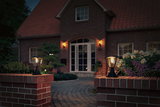 Two black metal outdoor lamps on red brick walls lighting a house entrance at dusk